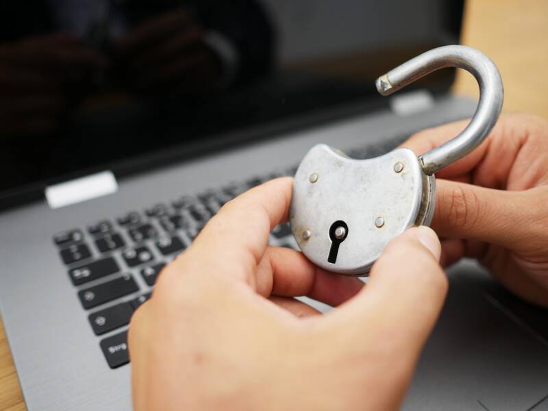Eine Person hält ein geöffnetes, großes Vorhängeschloss vor einem Laptop.